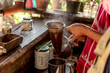 Traditional Thai coffee preparation using cloth filter in rural wooden kitchen. Close-up of hands pouring hot coffee, highlighting cultural rituals and slow living lifestyle in Asia.