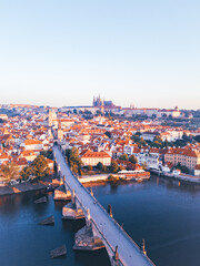 Obraz premium A breathtaking aerial view captures the medieval city of Prague at sunrise. The warm light highlights the Charles Bridge, Vltava River, and historic architecture, creating a serene morning atmosphere.