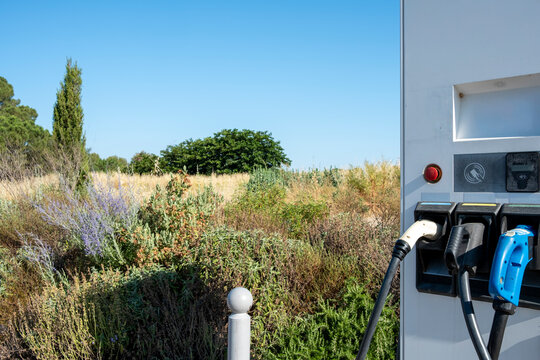 Rear view of dual electric charging units with black cables, countryside installation in Spain, dry vegetation and sustainability concept