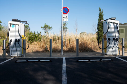 Dual electric car charging points under direct sunlight in countryside Spain, photographed from frontal angle showing parking infrastructure
