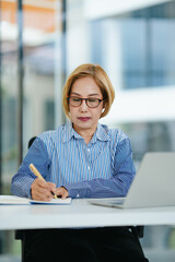 Middle aged asian woman working on documents data at contemporary office