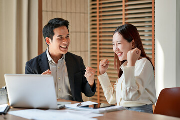 Business partners enjoy success moment while reviewing update on laptop in working space