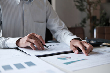 Male office staff analyzing accounting paperwork during financial review with attention to...
