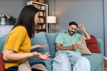 Relationship conflict between a jealous woman and her partner using a smartphone at home, illustrating communication problems, trust issues, emotional tension and digital distraction in couples