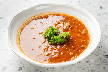 Bowl of tomato soup garnished with fresh parsley, served in a white dish on a speckled surface....