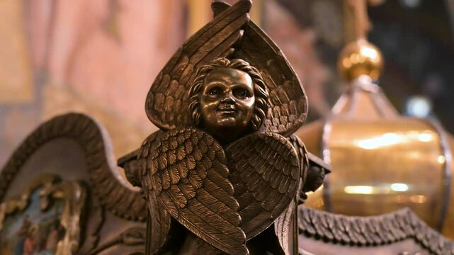 The detailed face and feathered wings of a cherub sculpture, a piece of sacred art within St. Volodymyr's Cathedral in Kyiv, Ukraine. This macro shot highlights the masterful carving of the ornament.