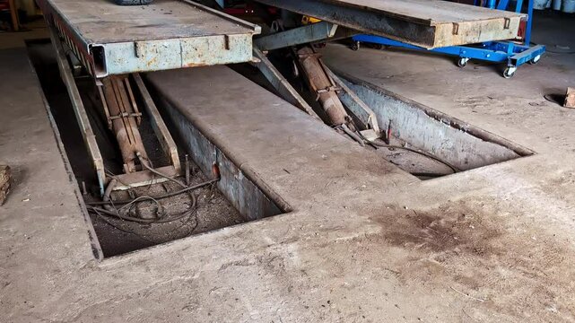 Hydraulic scissor lift platform lifts up with open pits in gritty auto workshop interior