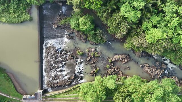 Aerial drone footage of a rocky river stream surrounded by lush green trees. The crystal-clear water flows gently between the stones, offering a peaceful, natural atmosphere.