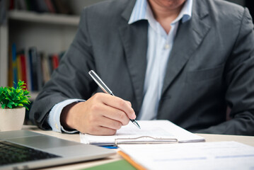 Businessman reviewing and signing a formal document at office desk. Ideal for concepts of legal agreement, business contract, and executive paperwork signing.