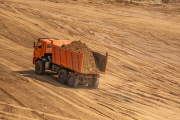 A loaded car drives out of a sand quarry. Sunny weather and clear skies