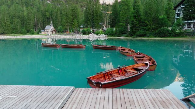 Lago di Braies or Lake Braies crystal blue lake with wooden rowing boats in Italian Dolomites, Lago di Braies chapel and coniferous and broadleaf trees in background, Closeup view