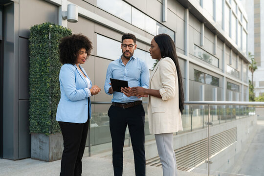 Three Multiracial business people discussing work strategy using a digital tablet outside office - Powered by Adobe