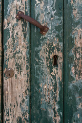 Close-up of weathered green door with peeling paint and rusty handle