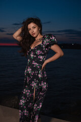 Woman in dress posing standing at pier near sea at the evening