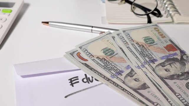 A student reveals a stack of cash prepared for tuition or school costs, with a white envelope marked "Education" placed neatly on a study desk &mdash; representing budgeting, savings, and financial planning