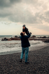 Father lifting laughing son at pebble beach with stormy sea and cloudy sky