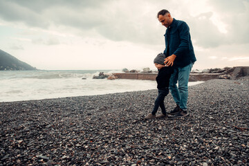 Father helping son walking on pebble beach on windy day
