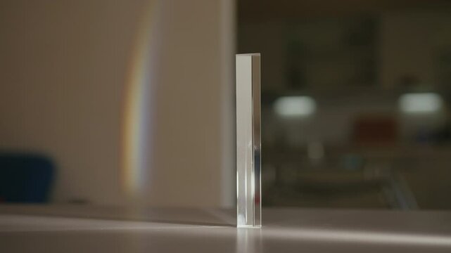 Light refracting through triangular glass prism, creating beautiful rainbow spectrum projected on wall at home in dark room. Concept principles of optics and light dispersion. Shooting in slow motion.