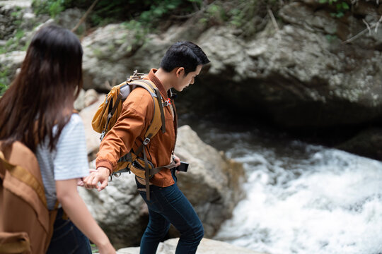 Hiking Together. Young couple navigating rocky terrain near a flowing river, enjoying nature.