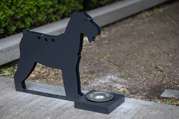 Metal dog-shaped water station with stainless steel bowl on city sidewalk, providing hydration for...