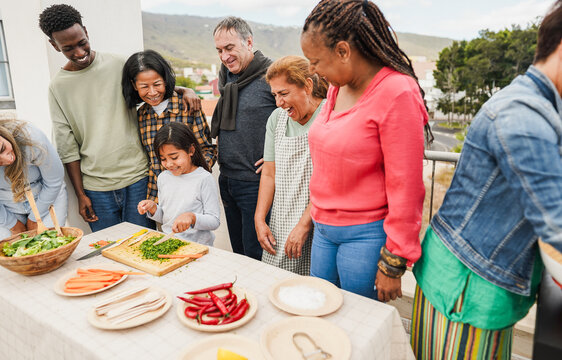 Multi generational people doing barbecue at home's rooftop - Multiracial friends having fun eating and cooking during weekend day - Summer and food concept - Main focus on kid face - Powered by Adobe