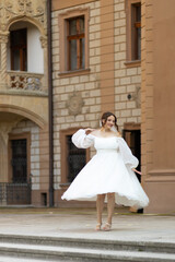 A bride in a voluptuous short dress spins against the backdrop of a historic building. Outdoor...