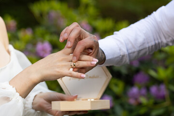 The groom puts a ring on the bride's finger against the background of blooming flowers. The groom...