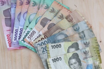 Pile of Indonesia rupiah money with various denominations on wooden table.

