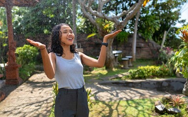 Joyful young Asian woman embracing the moment in a tropical garden mist. A refreshing and...
