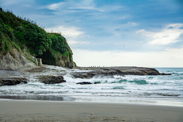 Sunset at Muriwai beach with waves splashing against the rocks and fishermen silhouettes in the distance. Auckland, New Zealand
