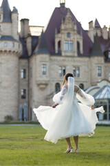 Obraz premium A bride in a fluffy white dress dances against the backdrop of the historic Moszna Castle. The bride's white dress and veil are flying.