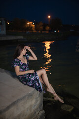 Woman in dress sitting at pier near sea at the night
