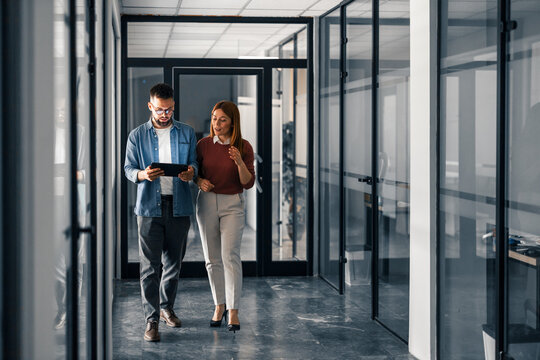 Colleagues Discuss Work While Walking Through Modern Office Hallway