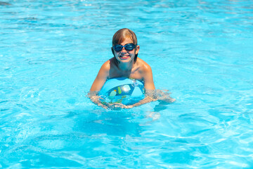 Naklejka premium smiling boy in glasses swimming on Inflatable ball with cheerful face, having fun on Summer travel hotel vacation, Kid relaxing in pool. swimming in blue water. activity, water sport.