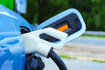 Close-up of an electric charger connected to a blue electric vehicle. Clean energy concept and the transition to green transportation.
