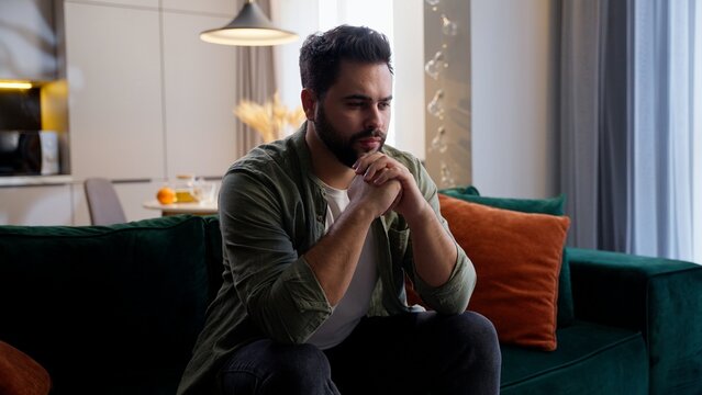Nervous thoughtful Caucasian business man male guy client homeowner businessman sitting sofa folded hands think deep difficult thoughts stress decision burnout mental health problems home living room
