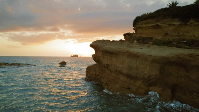 Sun setting behind a rocky cliff over the ocean with warm glowing reflections