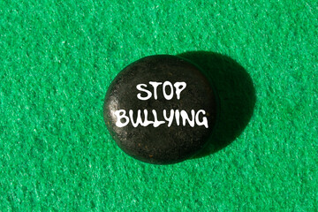 Stop bullying message written on black stone on green background. Conceptual stop bullying symbol....