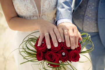 Brautpaar mit Eheringen und Brautstrauß aus roten Rosen – Hochzeitsfoto am Strand