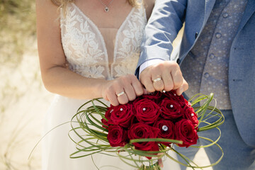 Brautpaar mit Eheringen und Brautstrauß aus roten Rosen – Hochzeitsfoto am Strand