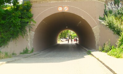 A short tunnel lined with bricks, a passage, with green trees and grass in front, and on the other...