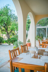 Outdoor patio with wooden tables and chairs in garden restaurant in Greece