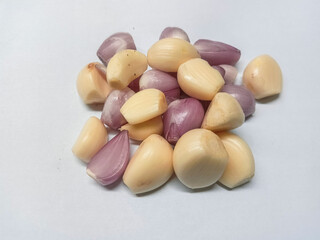 a pile of peeled garlic cloves and peeled shallots on a plain white surface