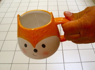 A man's hand holds a fox-shaped mug against a white background.