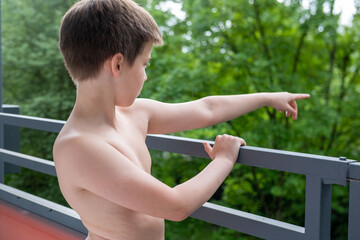 Young Shirtless boy standing on terrace, balcony, pointing into forest, enjoying fresh air...