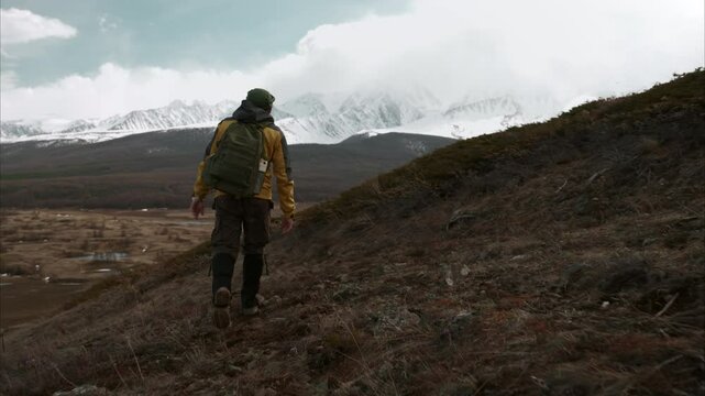 View from the back of hiker solo walking across a slope against the backdrop of high snowy Altai mountains. Perseverance, personal achievement, loneliness, freedom, wilderness exploration