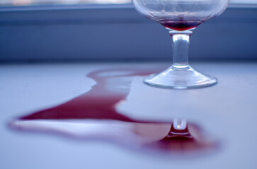 A glass and spilled red wine on the windowsill