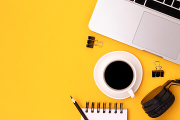 Stationery, laptop, cup of coffee and headphones on a yellow background. Place for text.