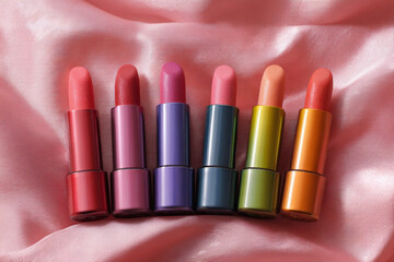 Obraz premium Vibrant collection of lipsticks displayed on soft satin fabric in pastel colors
