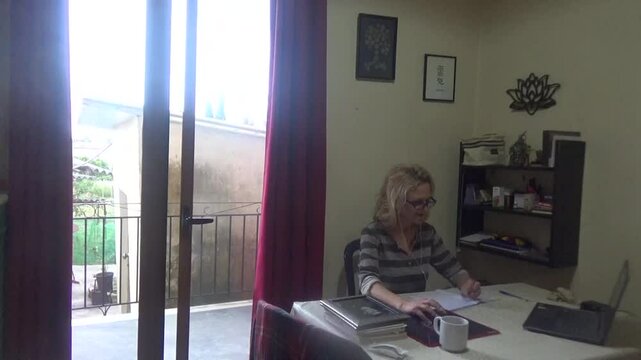 A cheerful woman in headphones and in a good mood is listening and watching videos on the computer. She is smiling and drinking hot chocolate. Daily life of a positive modern woman